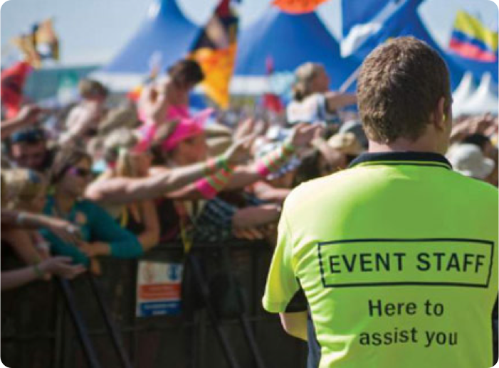 a music festival with corwd with colorful tents and flags in the background with an event security member in the forground 