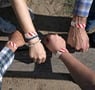 Group of people wearing red and white striped Tyvek event wristbands while reaching fists together outdoors on a wooden bench in sunlight.
