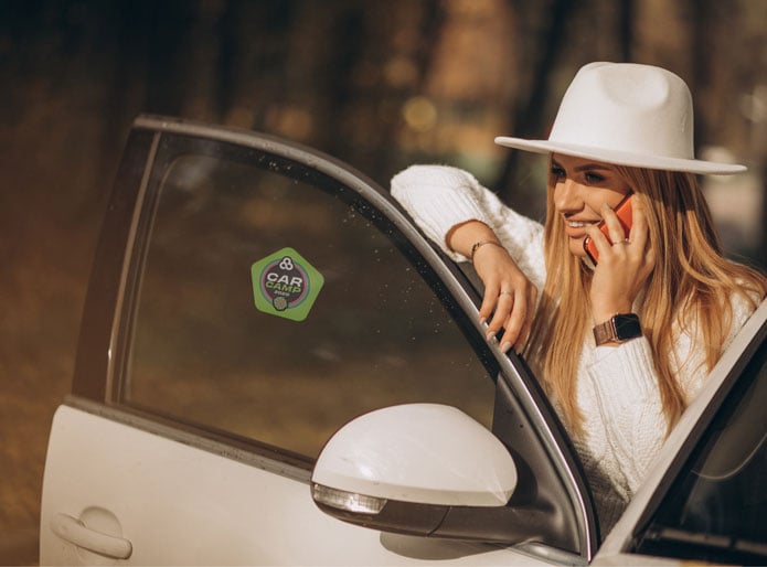a bohemian lady on the phone standing by her car that displays a green security sticker for parking lot access to an event