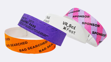 Assorted Tyvek wristbands in orange, purple, white, and pink, printed with event labels like &ldquo;ENTRY PASS&rdquo; and &ldquo;SPONSOR,&rdquo; showing customisation and single-use features for short-term events